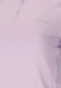 Close-up van een lichtroze sporttop met korte rits en "ENDURANCE"-logo op de borst, voorzien van mesh-details aan de zijkanten.