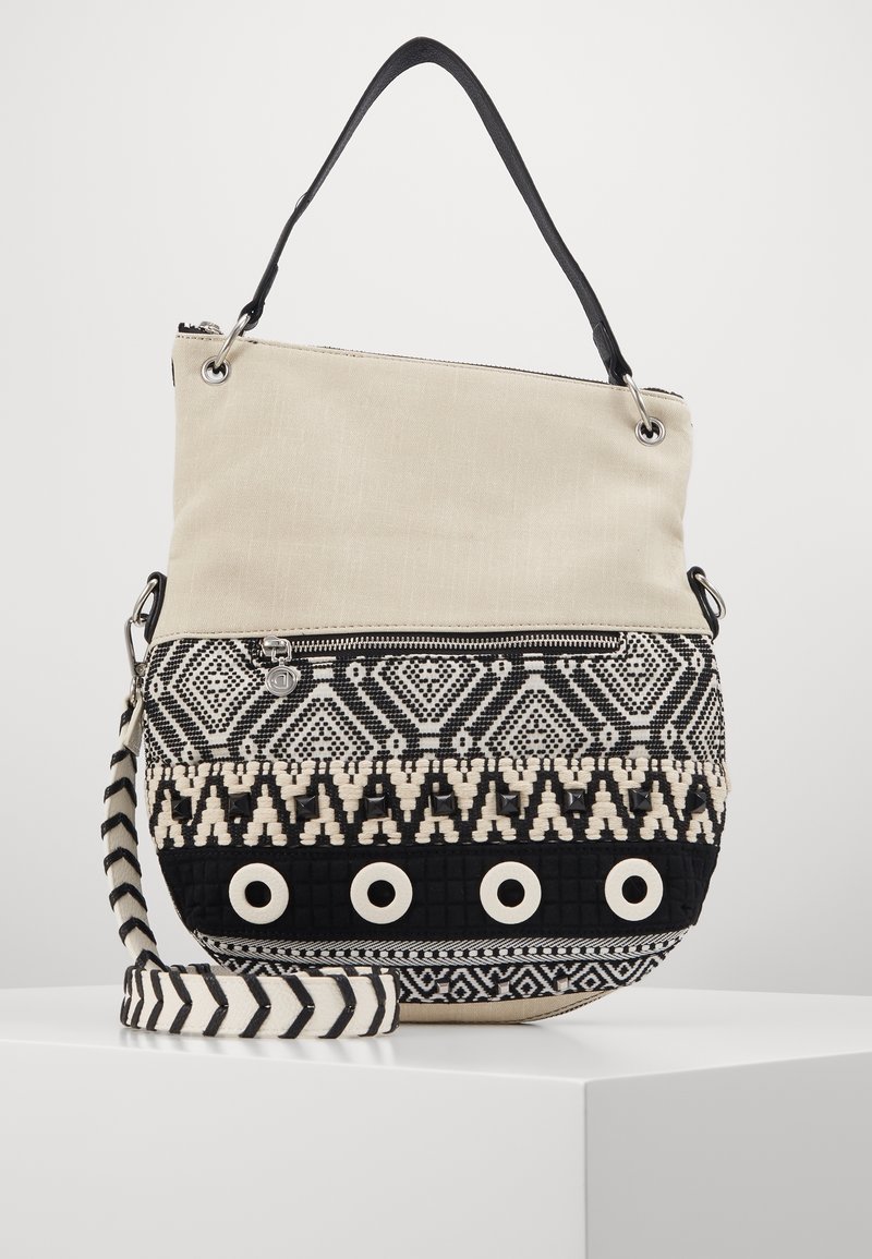 Torba na ramię z płótna i tkanej tkaniny w kolorze beżowym i czarnym. Posiada geometryczne wzory i okrągłe akcenty; zawiera regulowany paski w paski.