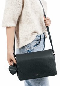 Black leather handbag with a textured finish, featuring a detachable heart-shaped keychain. The bag has a flap closure and a long shoulder strap.
