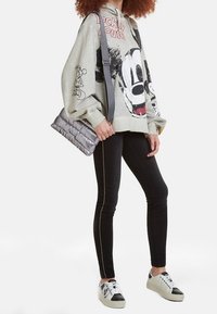 Szara, oversize'owa bluza z nadrukiem Myszki Miki, zestawiona z czarnymi jeansami z żółtym przeszyciem po bokach oraz czarno-białymi trampkami.