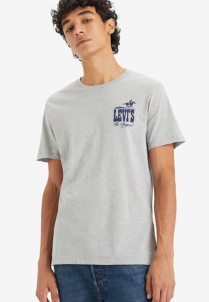 Camiseta de algodón gris con un logotipo de Levi's en navy en el lado izquierdo del pecho. Mangas cortas y cuello redondo. Diseño simple y casual.