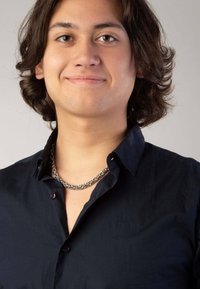 Zwarte button-up blouse met een gegraveerde zilveren kettinghalsband. Geweven stof zichtbaar; model heeft schouderlang golvend haar.