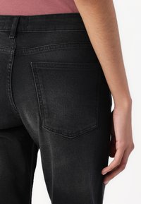 Blugi din denim negru cu un design ajustat, având buzunare la spate și o textură netedă, cu detalii subtile de cusătură pe margini.