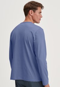 Blauwe langslijfshirt van zachte stof, relaxte pasvorm, ronde halslijn, met manchetten bij de polsen. Patroonschoenen zichtbaar hieronder.