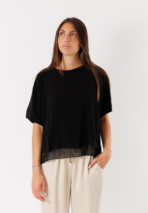 Top nero a maniche corte con l'orlo inferiore trasparente e setoso, abbinato a pantaloni beige chiari e morbidi. Taglio semplice, rilassato e tessuto morbido.