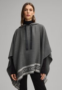 Poncho grigio a maglia con cappuccio, dotato di cordini neri. L'orlo include una banda decorativa con il marchio "JOOP!". Texture morbida.