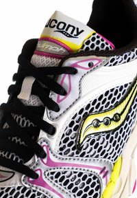 Sneaker a rete in bianco e nero con accenti gialli e rosa, caratterizzata da un design testurizzato, un logo prominente e lacci neri.