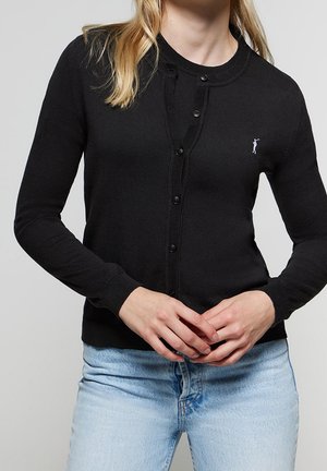 Cardigan noir en tissu doux, avec un col rond, des boutons et des poignets côtelés. Petit détail de logo sur la poitrine gauche.