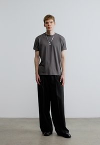 Camiseta gris de manga corta y pantalones negros de pierna ancha. Modelo con collar plateado. Tejido liso con corte holgado. Diseño minimalista.