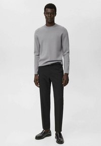Grauer Strickpullover mit Rundhalsausschnitt, kombiniert mit maßgeschneiderten schwarzen Hosen und schwarzen Schuhen. Der Stoff ist glatt mit einer subtilen Textur.