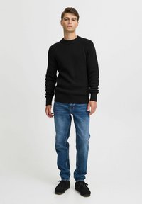 Pulover negru, din tricot cu model listat, cu guler rotund, asortat cu blugi bleu din denim și pantofi negri. Design simplu și croială clasică.