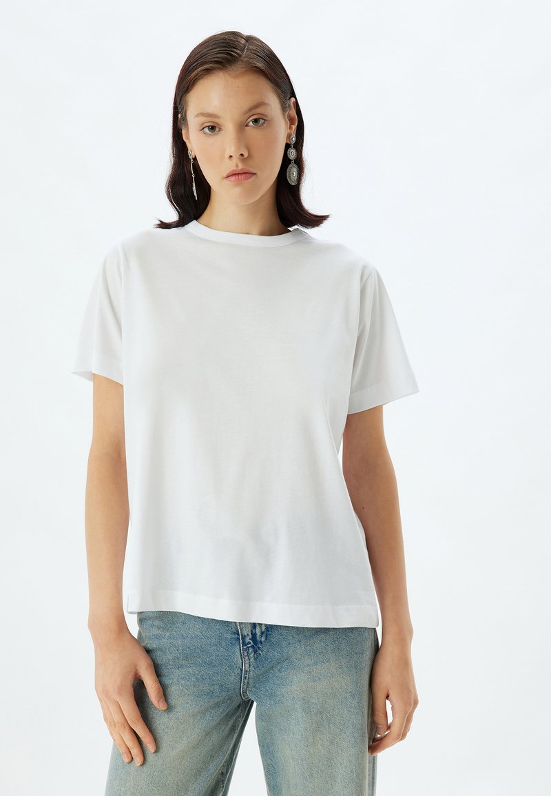 Hvid bomulds t-shirt med rund hals, korte ærmer og afslappet pasform, parret med lyseblå denim jeans. Enkel og minimalistisk design.