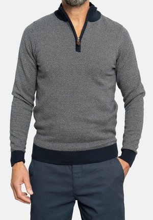 Suéter de punto en navy y gris con cuello con cremallera, patrón texturizado y puños y cintura acanalados. La tela parece suave y elástica.
