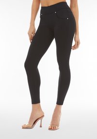 Musta korkeavyötäröiset leggingsit, joissa on sileä pinta, tekotaskut edessä ja hopeiset yksityiskohdat, yhdistettynä läpikuultaviin korkeakorkoisiin sandaaleihin.