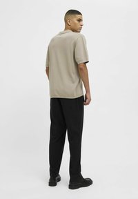 Beige polo shirt met korte mouwen en een relaxte pasvorm, gecombineerd met zwarte broeken en zwarte schoenen, gezien vanaf de achterkant. Smooth textuur.