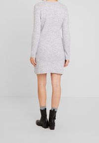 Abito in maglia grigia a coste con maniche lunghe, scollatura rotonda e spacchi laterali, abbinato a stivali neri alla caviglia e calzini grigi.