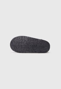 Suela de zapato de goma negra con superficie texturizada que presenta patrones abstractos y ranuras para tracción. Diseño plano, color uniforme en toda la suela.