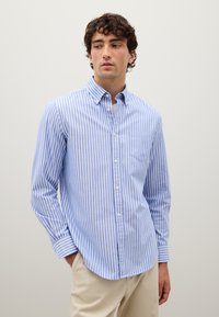 Camisa de botón de manga larga a rayas en azul claro y blanco, con cuello abotonado, que presenta un bolsillo en el pecho y mangas con puños.