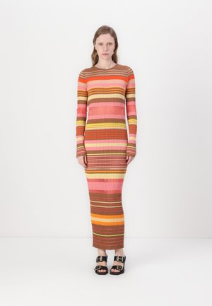 Kudotun maxi elbise, pembe, turuncu, kahverengi ve sarı yatay çizgiler içeriyor. Uzun kollar, ribana dokusu ve yuvarlak yaka. Siyah sandaletler.