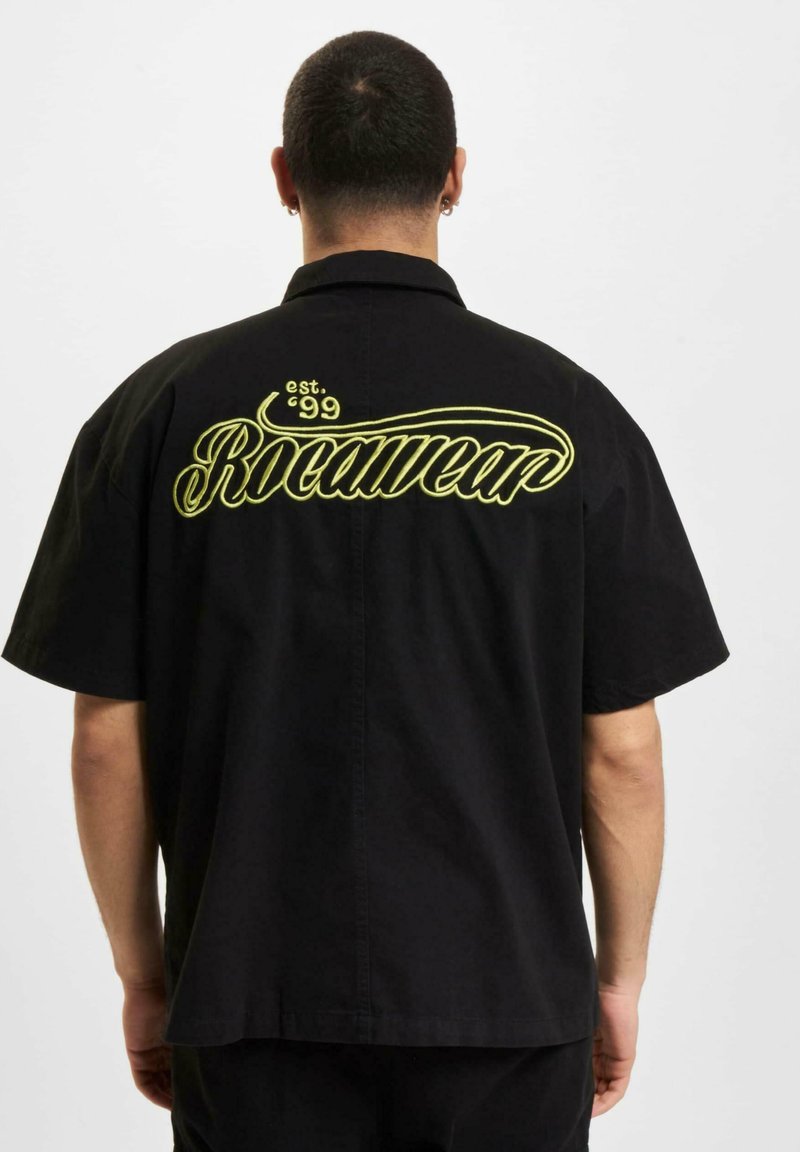 Fekete rövid ujjú póló, amelyen nagy sárga "Rocawear" logó és "est. '99" hímzés található a hátán; laza fazon, kényelmes illeszkedéssel.