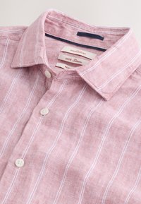 Linneskjorta i ljusrosa med vita vertikala ränder. Har en knappkrage och två knappar på knäppningen. Etiketterna är synliga.