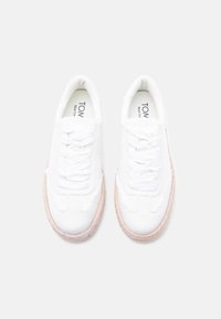 Λευκά sneakers από καμβά με υφασμένους ανοιχτό μπεζ πάτους, χαρακτηριστικά στρογγυλά κορδόνια και ραφές κατά μήκος των πλευρών.