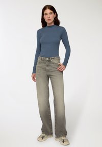 Długi rękaw, wysoki kołnierz, niebieska bluzka w połączeniu z jasnoszarymi, szerokimi dżinsami o wyblakłej teksturze i subtelnych detalach metalowych.