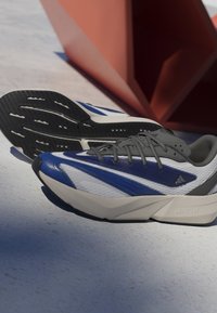Blue and white athletic shoes with gray accents, breathable mesh upper, black rubber sole, featuring a prominent brand logo and "LIGHTSTRIKE" detail.