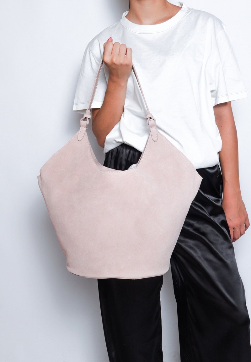 Borsa a tracolla in suede rosa chiaro con un'ampia apertura e doppi manici. Presenta un fondo arrotondato e una superficie liscia.