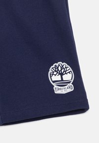 Marineblaues Baumwoll-T-Shirt mit einem weißen Timberland-Logo, das eine Baum-Silhouette zeigt, in einem kreisförmigen Design, und dem Text "Established 1973". Glatte Textur.