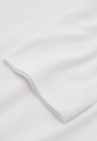 Witte ribstof met een gevouwen randdetail, met een close-up van de textuur en het zachte materiaal.