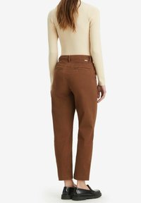 Brązowe bawełniane spodnie o luźnym kroju, z tylnymi kieszeniami i skróconym dołem. Noszone z beżową bluzką z długim rękawem i czarnymi butami.