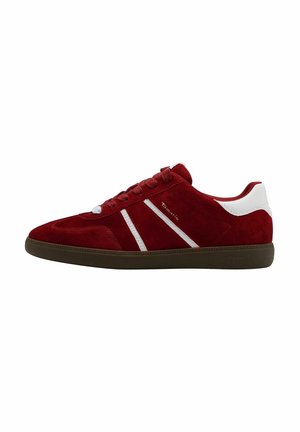 Czerwony zamszowy sneaker z białymi paskami, białą naszywką na pięcie, sznurowadłami i ciemnobrązową podeszwą, widok z boku.