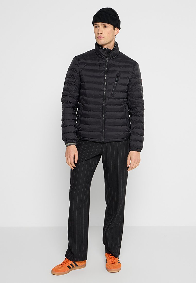 Zwarte gewatteerde jas met een staande kraag, horizontaal gestikt ontwerp, rits aan de voorkant en een klein ritsvakje op de borst, gecombineerd met verticaal gestreepte broek.