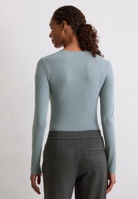 Langsleeve, lichtblauw top met een aansluitend ontwerp, gecombineerd met donkergrijze, elastische taillebandbroeken met zijritsen en zakken.