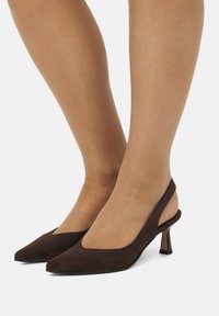 Tacchi slingback in suede marrone con punta affusolata e tacco a stiletto piccolo. Presentano una texture liscia e un taglio a forma di V sui lati.