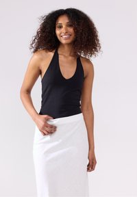 Sort halterneck-top med en dyb udskæring, parret med en hvid knælang nederdel med et tekstureret mønster. Halvlangt krøllet hår synligt.