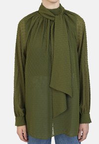 Olive green blouse with a high neck, gathered detailing, and a front tie. Features textured dots, long sleeves, and a loose silhouette.
