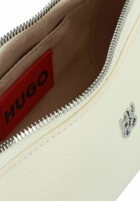 Funda de cuero blanco con cremallera plateada y detalle del logotipo. El interior es beige con una etiqueta de marca roja visible. Textura suave y diseño sencillo.