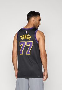 Camisola de basquetebol preta com detalhes em roxo. Texto nas costas: "DONČIĆ" e "77" em amarelo. Apresenta uma textura de tecido típica de vestuário desportivo.