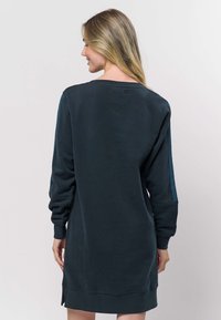 Dunkelblaues Sweatshirtkleid mit langen Ärmeln, gerippten Bündchen und seitlichen Schlitzen. Glatte Textur und entspannte Passform, mit rundem Ausschnitt.