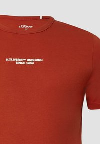 T-shirt rossa in cotone con collo a giro, maniche corte e testo bianco che reca la scritta "s.Oliver® UNBOUND SINCE 1969" sul davanti.