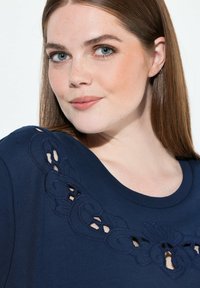 Sudadera azul marino con bordados intrincados y detalles troquelados en el escote. Textura suave y diseño de cuello redondo.