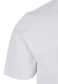 Läheltä kuvattu valkoinen puuvillapaita, joka esittelee kankaan sileän tekstuurin, lyhyet hihat ja pyöreän kaula-aukon. Minimalistinen muotoilu.