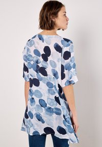 Lightweight, loose-fitting blouse made of textured fabric, featuring a blue and white large polka dot pattern and short sleeves.