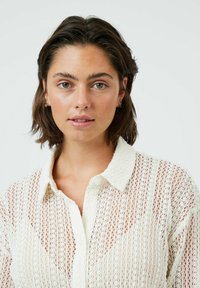 White, knitted button-up shirt with a textured pattern, featuring a collar and a slightly transparent fabric.