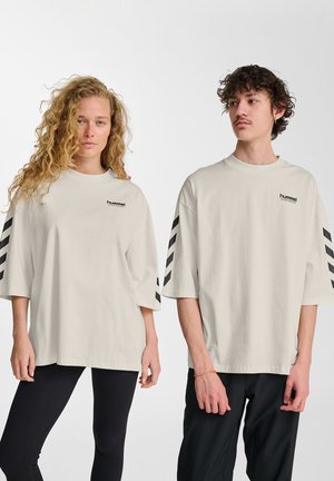 Lys beige oversized t-shirt med sorte stribede detaljer på ærmerne og et lille logo på brystet. Lavet af bomuldsstof, afslappet pasform.