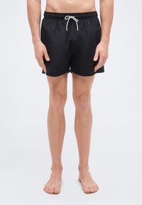 Μαύρο μαγιό σορτς κατασκευασμένο από ελαφρύ ύφασμα, με ελαστική μέση και κορδόνι, καθώς και πλαϊνές τσέπες με λείο υλικό.