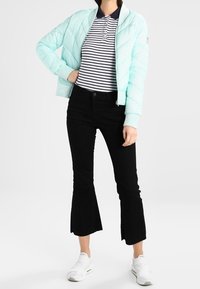 Světle modrá prošívaná bomber bunda, pruhované polo tričko, černé kordové zvonové kalhoty, bílé slip-on boty. Neformální, vrstvený outfit s barevným kontrastem.