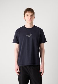 Námornícka modrá bavlnená tričko s krátkymi rukávmi, okrúhlym výstrihom a centrálne umiestneným bielym logom "Calvin Klein Jeans". Jednoduchý dizajn, voľný strih.